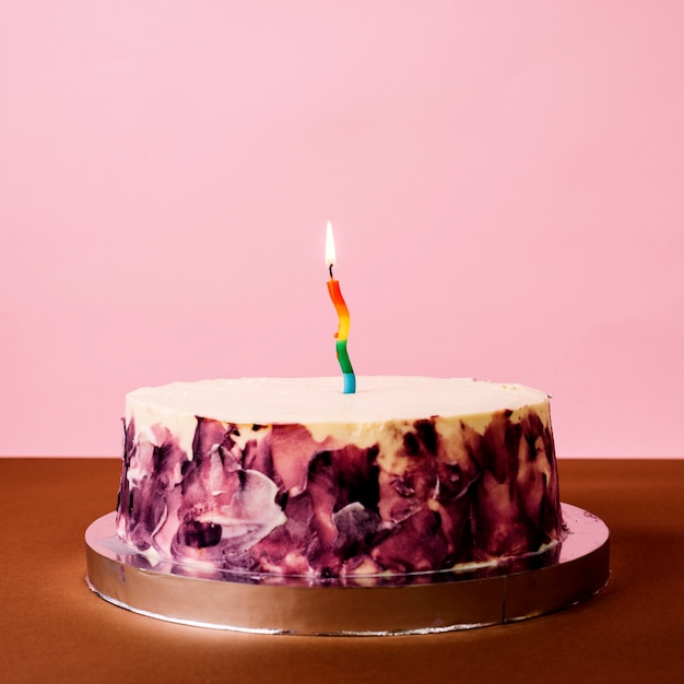 Красочная зажженная свеча на круглом торте за столом на розовом фоне