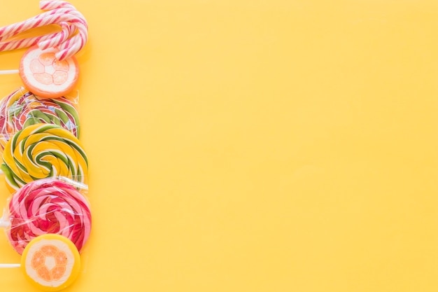 Colorful lollipops and christmas cane candies on yellow backdrop