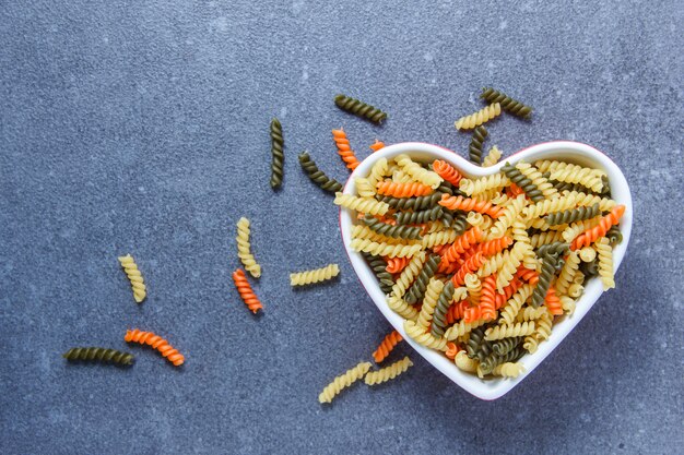 Colorful macaroni pasta in a heart shaped bowl on a gray surface