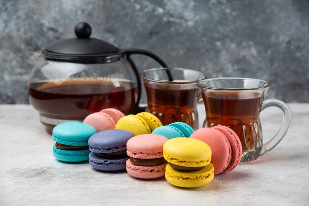 Colorful macarons with teacup and two cups of black tea on white surface.