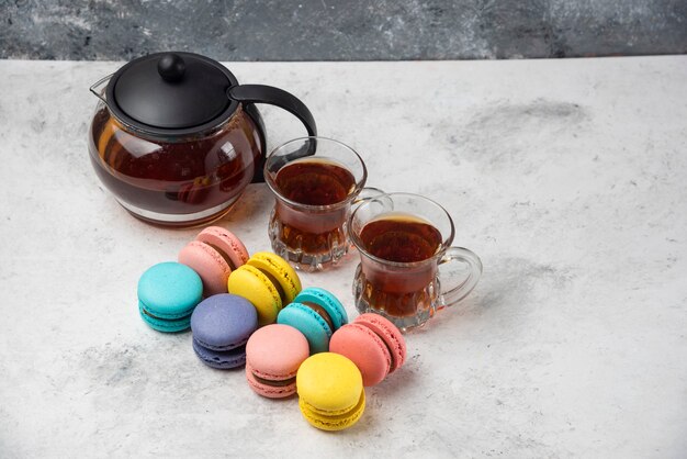 Colorful macarons with teacup and two cups of black tea on white surface.