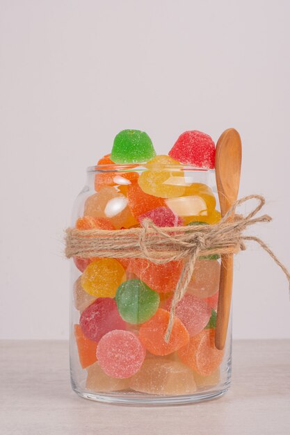 Colorful marmalades in glass jar with wooden spoon.