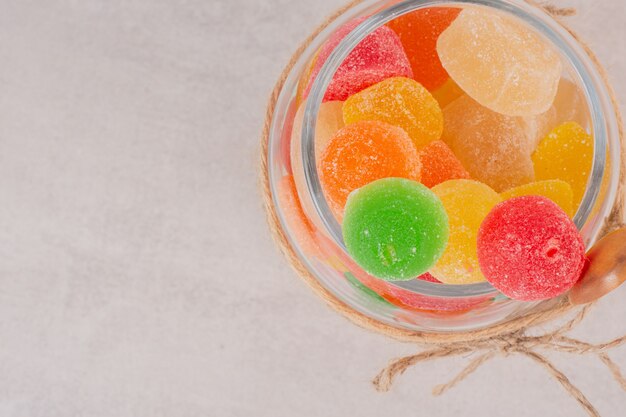 Colorful marmalades in glass jar with wooden spoon.