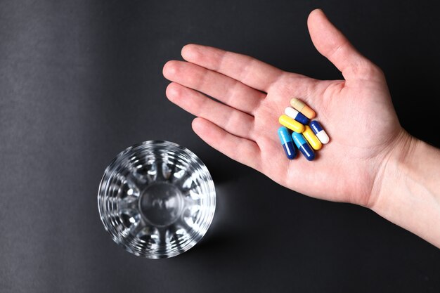 Colorful medical pills in the hand of a person and a glass of water. Top view.