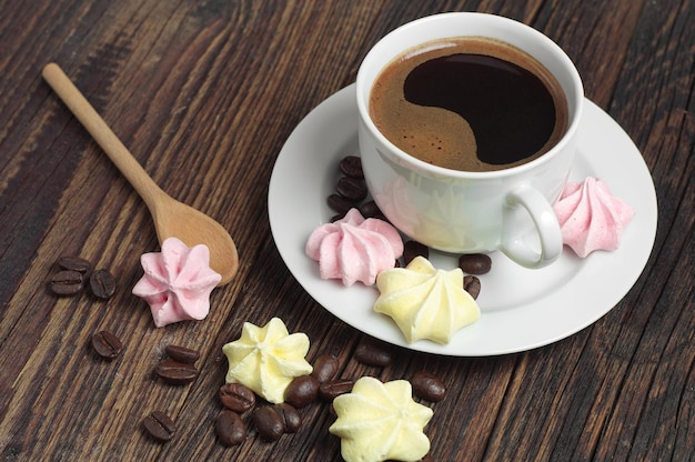 カラフルなメレンゲクッキーと素朴な木製テーブルの上のホットコーヒーのカップ