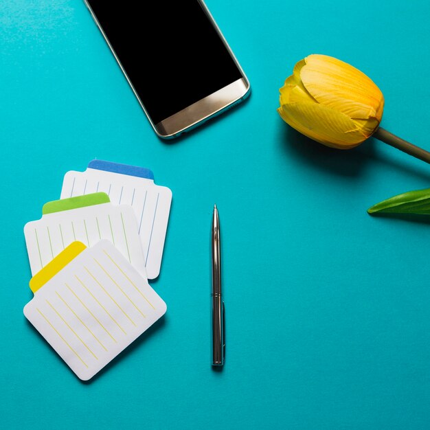 펜으로 다채로운 메모장; 파란색 배경에 휴대 전화 및 노란 튤립