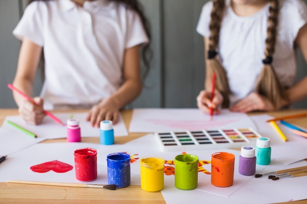 Разноцветные краски перед девушкой, рисующей на белой бумаге над столом