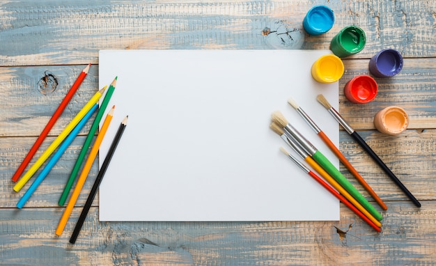 Colorful painting supplies with white blank paper over wooden background