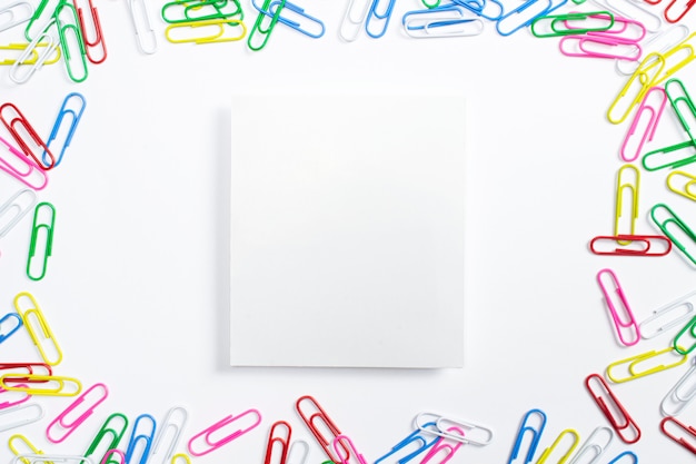 Free photo colorful paper clips and portrait paper frame in the centre of composition isolated on white.