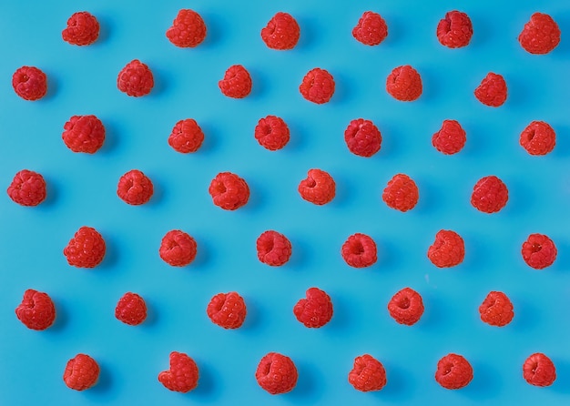 Colorful pattern of ripe raspberry berries on a bright blue background. Top view, berry background