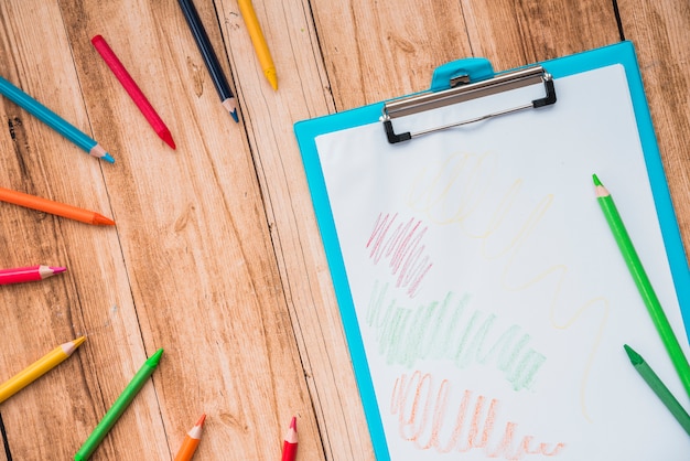 Colorful pencil and clipboard with white paper on wooden table