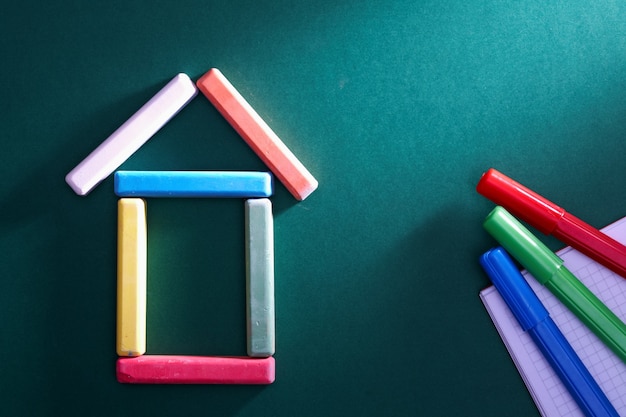 Colorful pieces of chalk put in form of house on blackboard