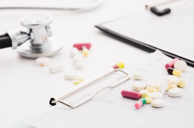 Colorful pills over the ecg graph and stethoscope on white background