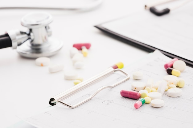Бесплатное фото Красочные таблетки на графике экг и стетоскоп на белом фоне