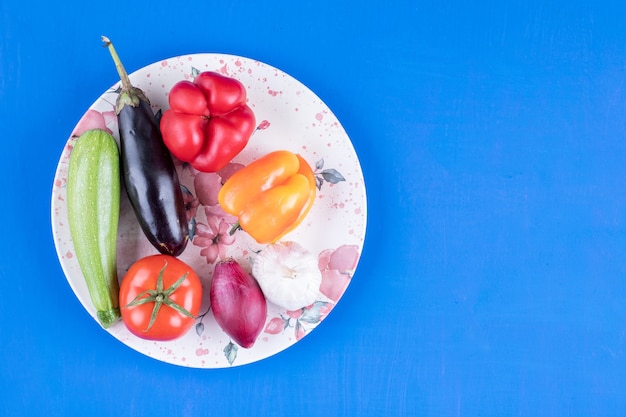 青いテーブルの上の新鮮な熟した野菜のカラフルなプレート。