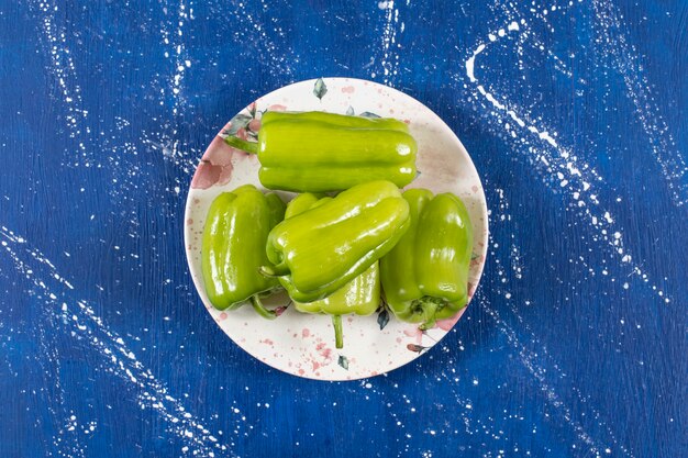 Colorful plate of green bell peppers on marble table.