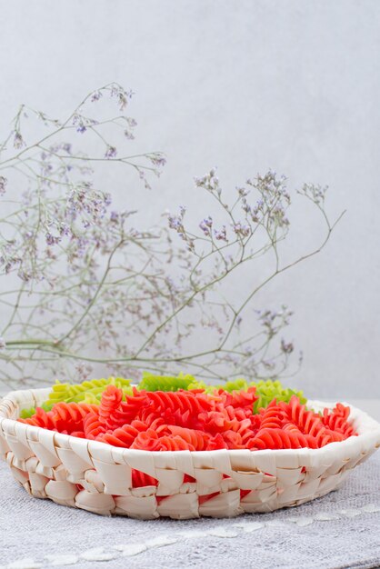 Colorful raw macaroni on plate with withered flower