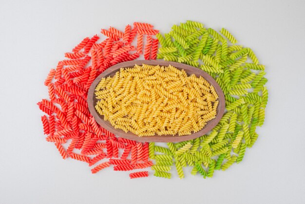 Colorful raw macaroni on white plate on white surface