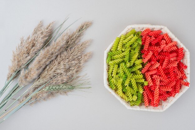 Colorful raw macaroni on white plate on white surface