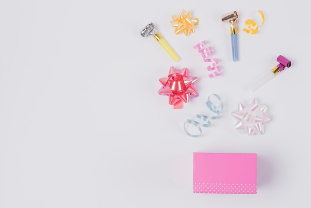 Free photo colorful ribbon bow; curling ribbon and blowing horns over the pink box against white background