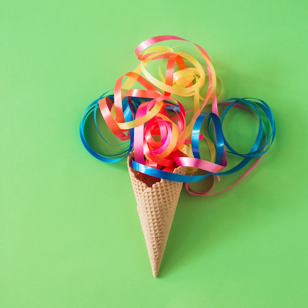 Colorful ribbons over waffle ice cream cone on green background