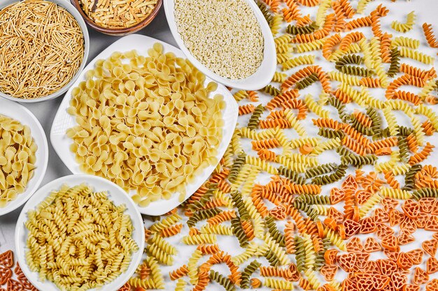 Colorful scattered fusilli and bowls of raw pastas on white background