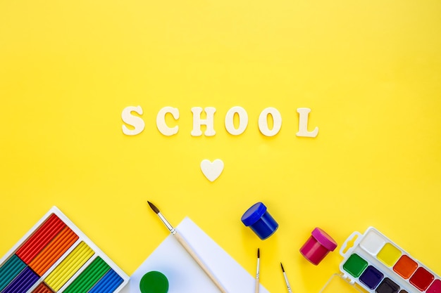 Free photo colorful school supplies and wooden letters on a yellow background back to school concept top view