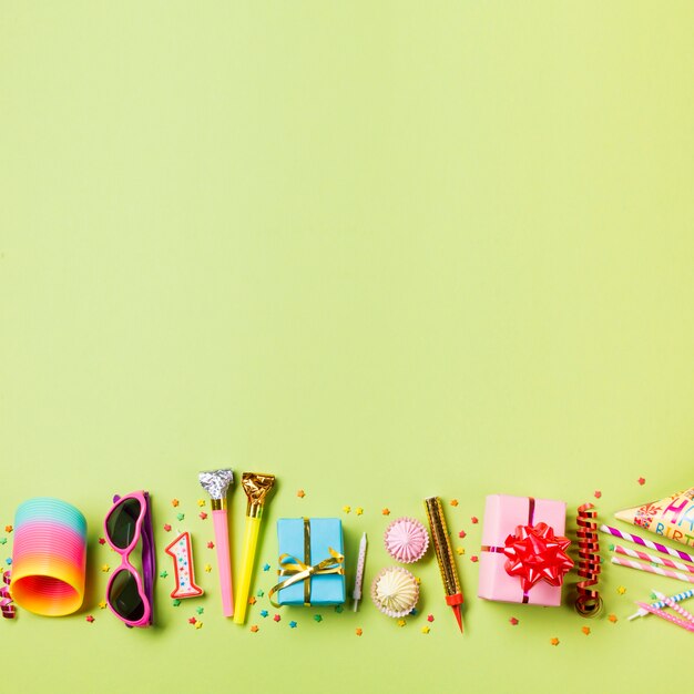 Colorful springs; sunglasses; candle; party horn; gift box; aalaw; streamer and drinking straws on the green backdrop