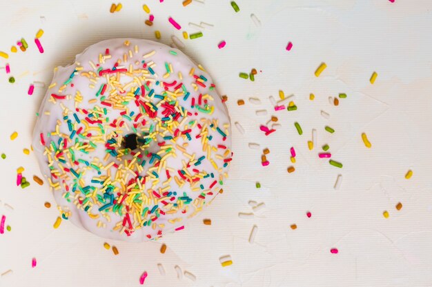 Colorful sprinkles over the white donut against white backdrop