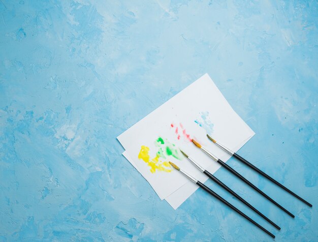 Colorful stained drawing paper with paint brush on blue background