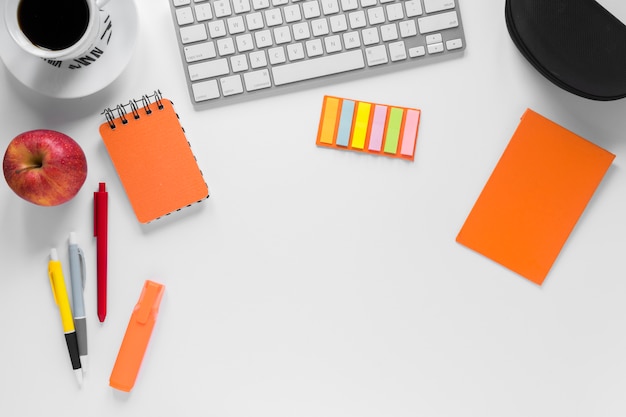 Colorful stationeries with coffee cup; apple and keyboard on white desk