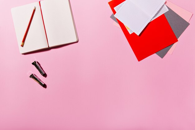 Colorful stationery and open note book are next to lipsticks on pink wall