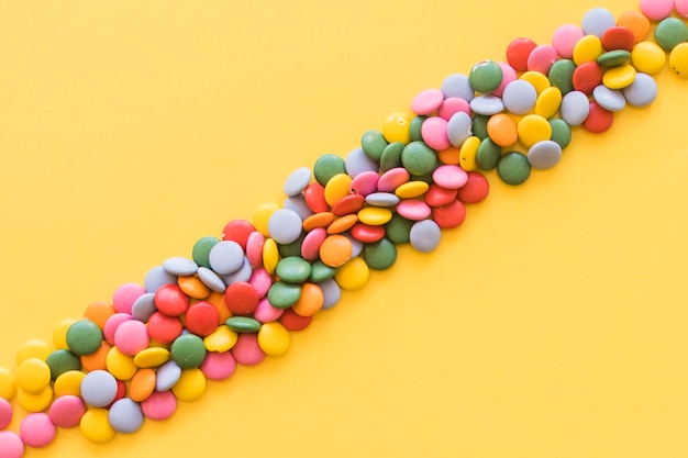 Colorful stripes of gems candies on yellow background