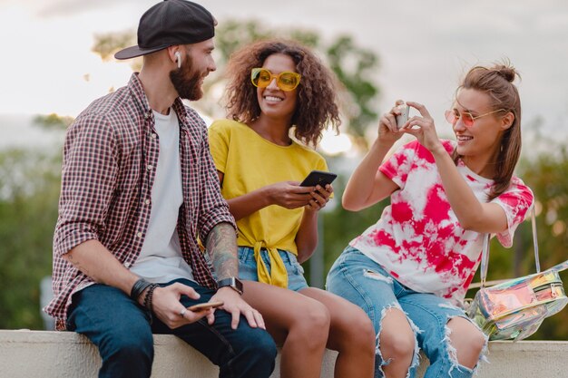 Foto gratuita colorata ed elegante felice giovane compagnia di amici seduti nel parco, uomo e donna che hanno divertimento insieme