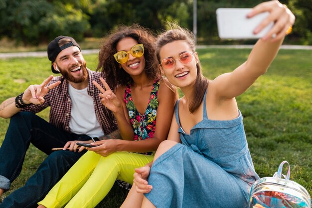 Красочная стильная счастливая молодая компания друзей, сидящих в парке, мужчины и женщины, весело проводящие время вместе