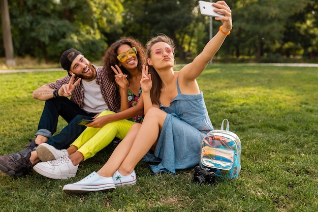 Красочная стильная счастливая молодая компания друзей, сидящих в парке, мужчины и женщины, весело проводящие время вместе