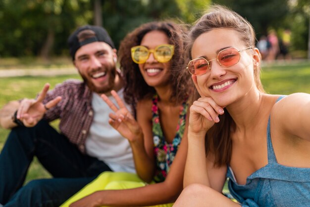 Colorful stylish happy young company of friends sitting park, man and women having fun together