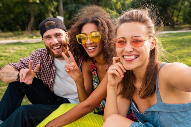 Colorful stylish happy young company of friends sitting park, man and women having fun together