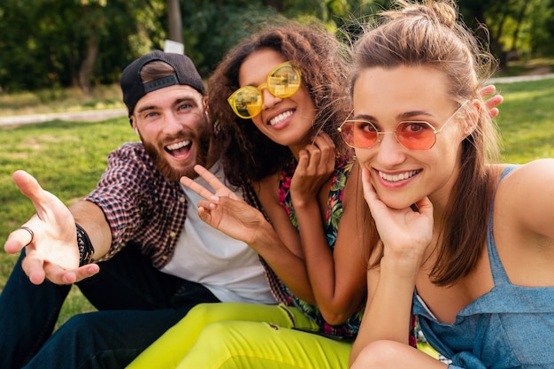 Colorato elegante felice giovane compagnia di amici seduti parco, uomo e donna che hanno divertimento insieme