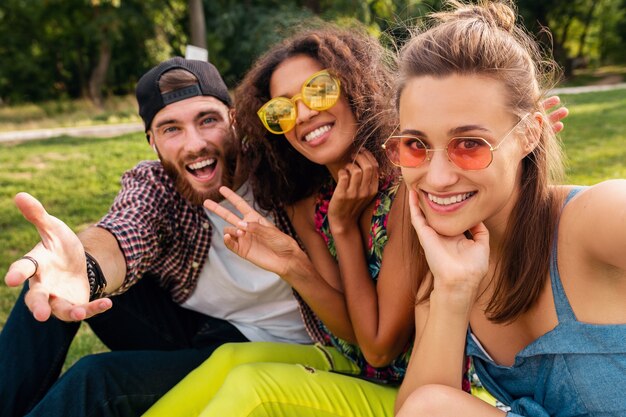 Colorful stylish happy young company of friends sitting park, man and women having fun together