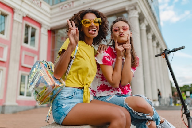 Amici di ragazze giovani felici alla moda colorati sorridente seduto in strada, donne che si divertono insieme