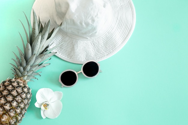 Colorful summer female fashion outfit flat-lay.White stylish women's hat with sunglasses and fresh pineapple . Summer fashion or holiday travel concept