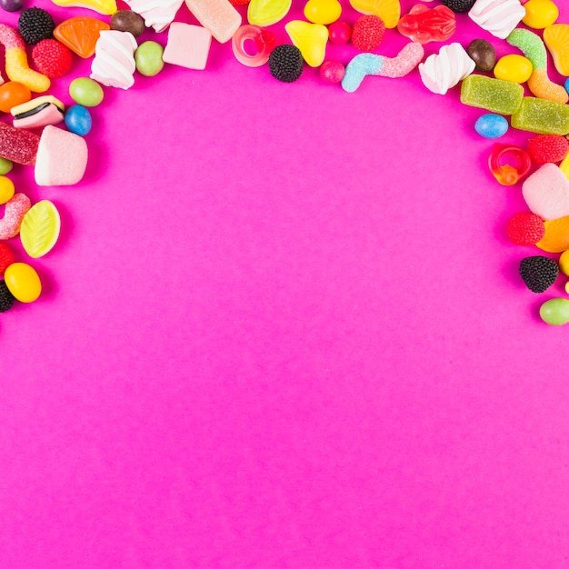 Colorful sweet candies forming arch shape on pink backdrop