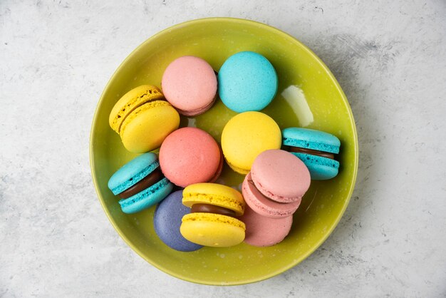 Colorful tasty macarons on green plate and on white table. 