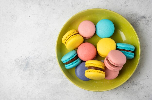 Colorful tasty macarons on green plate and on white table. 