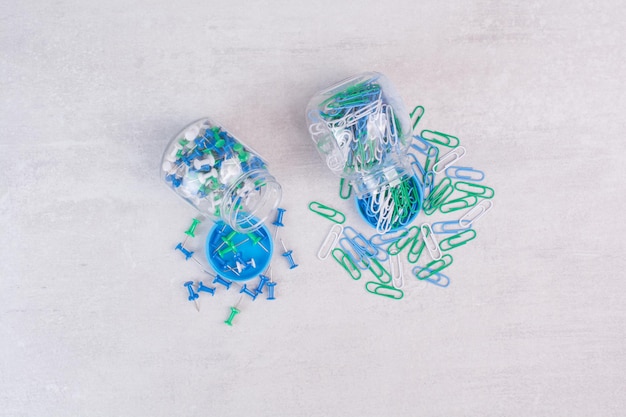 Free photo colorful thumbtacks in two glass jars on white table.