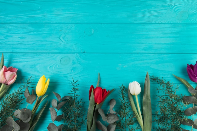 Foto gratuita tulipani variopinti e foglie verdi sul contesto di legno del turchese