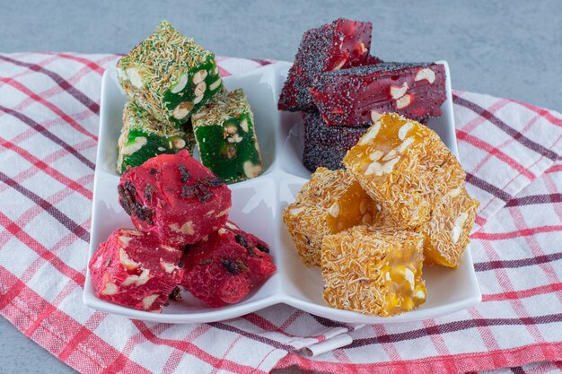 Colorful Turkish delight flavors on a bowl, on the tea towel, on marble table. 