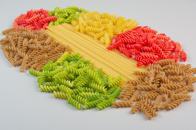 Colorful uncooked spiral pasta and spaghetti on white surface.