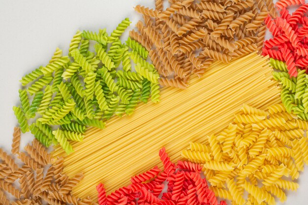 Colorful uncooked spiral pasta and spaghetti on white surface